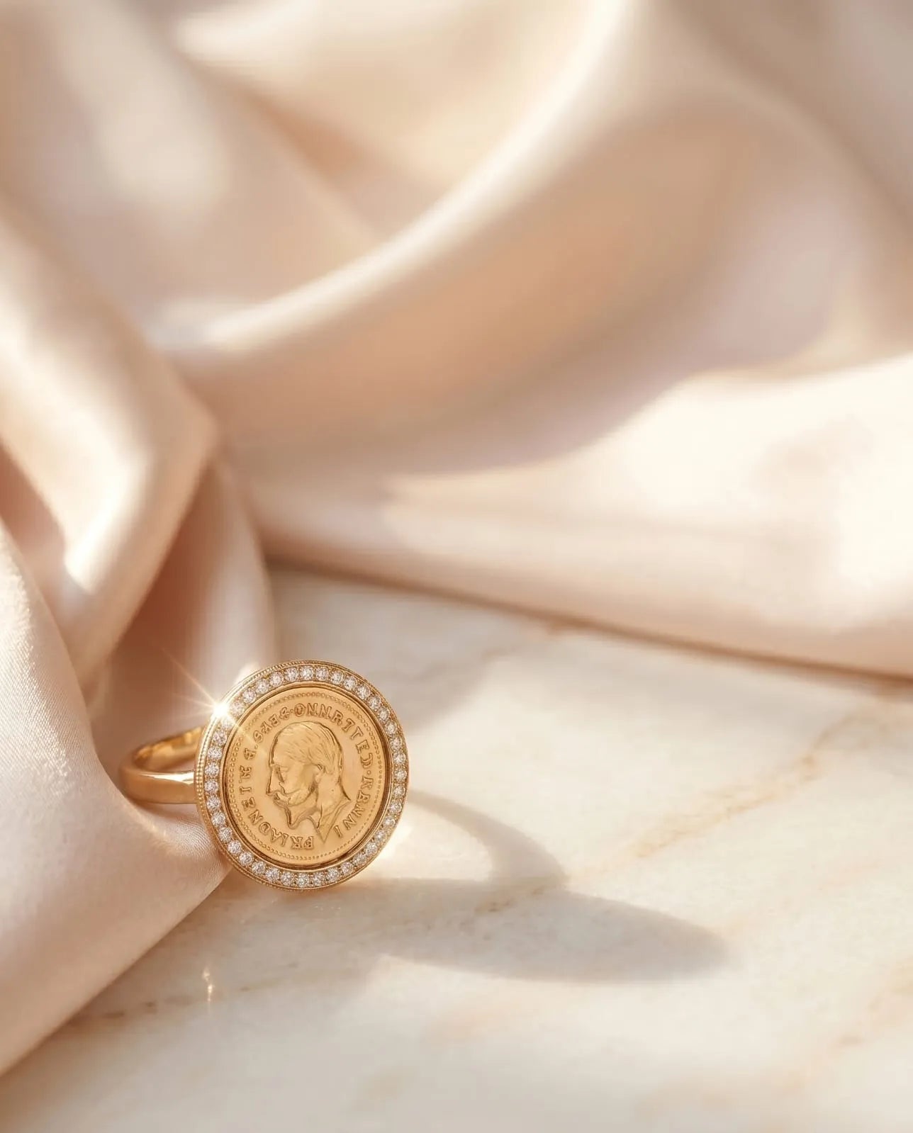 Close up of a luxury gold-plated statement ring from Bellora Bloom featuring a classic engraved Lira coin medallion framed with sparkling zircon crystals resting on smooth satin fabric.