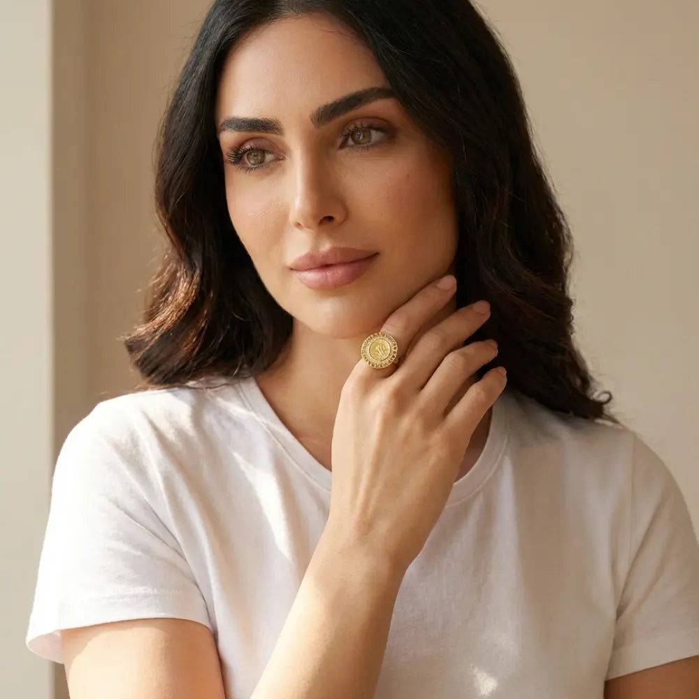 Woman wearing a gold ring, posing with hand by her face against a neutral background