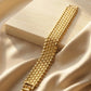 Close up of a luxury gold-plated classic broad bracelet from Bellora Bloom featuring a textured metallic mesh design resting on smooth satin fabric.