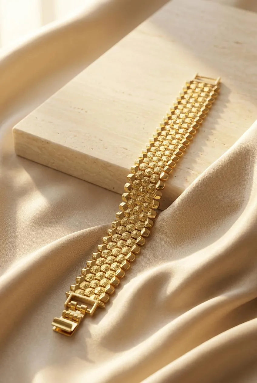 Close up of a luxury gold-plated classic broad bracelet from Bellora Bloom featuring a textured metallic mesh design resting on smooth satin fabric.