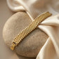 Close up of a luxury gold-plated classic broad bracelet from Bellora Bloom featuring a textured metallic mesh design resting on smooth satin fabric.