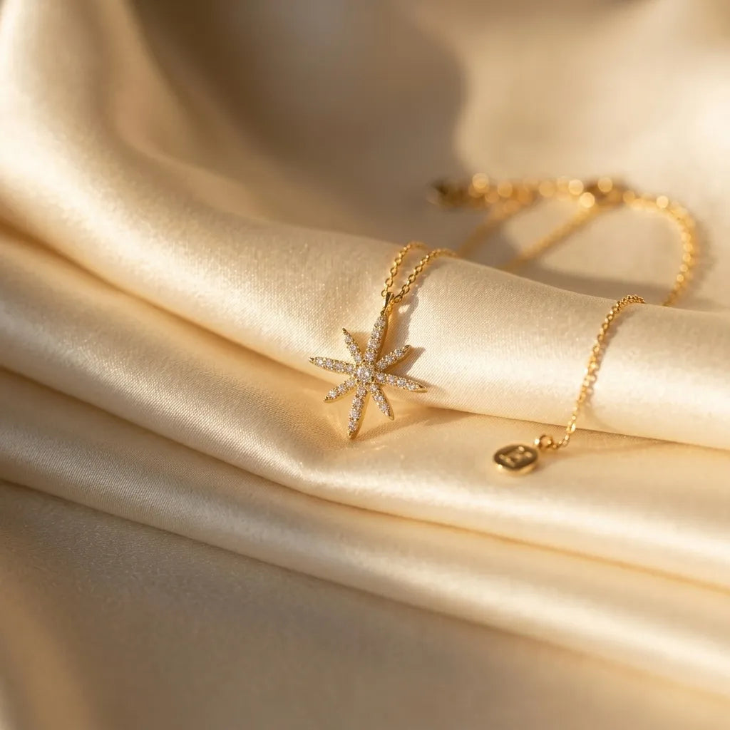 Close up of a luxury gold-plated necklace from Bellora Bloom featuring a celestial radiant starburst pendant paved with sparkling zircon crystals resting on smooth satin fabric.