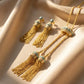 Gold tassel earrings with turquoise stones on a beige fabric background