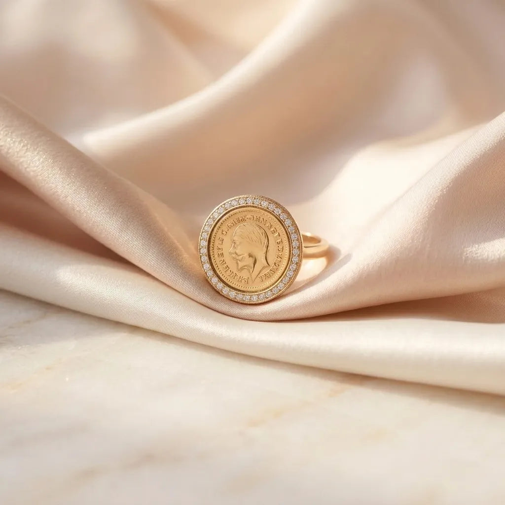 Close up of a luxury gold-plated statement ring from Bellora Bloom featuring a classic engraved Lira coin medallion framed with sparkling zircon crystals resting on smooth satin fabric.