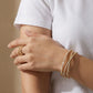 Close-up of a woman's hand wearing stacked thin gold bracelets and a bold encrusted gold ring.