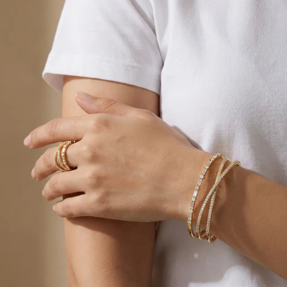 Close-up of a woman's hand wearing stacked thin gold bracelets and a bold encrusted gold ring.