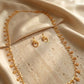 Close up of a luxury gold-plated new arrival long necklace and matching earrings set from Bellora Bloom featuring authentic Khaliji motifs resting on smooth satin fabric and stone display.