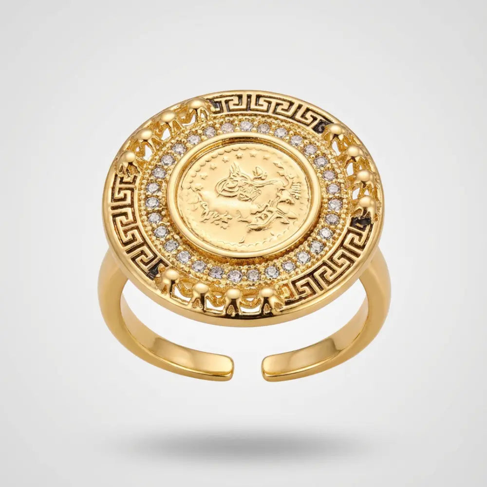 Gold ring with a coin design and gemstones on a light gray background