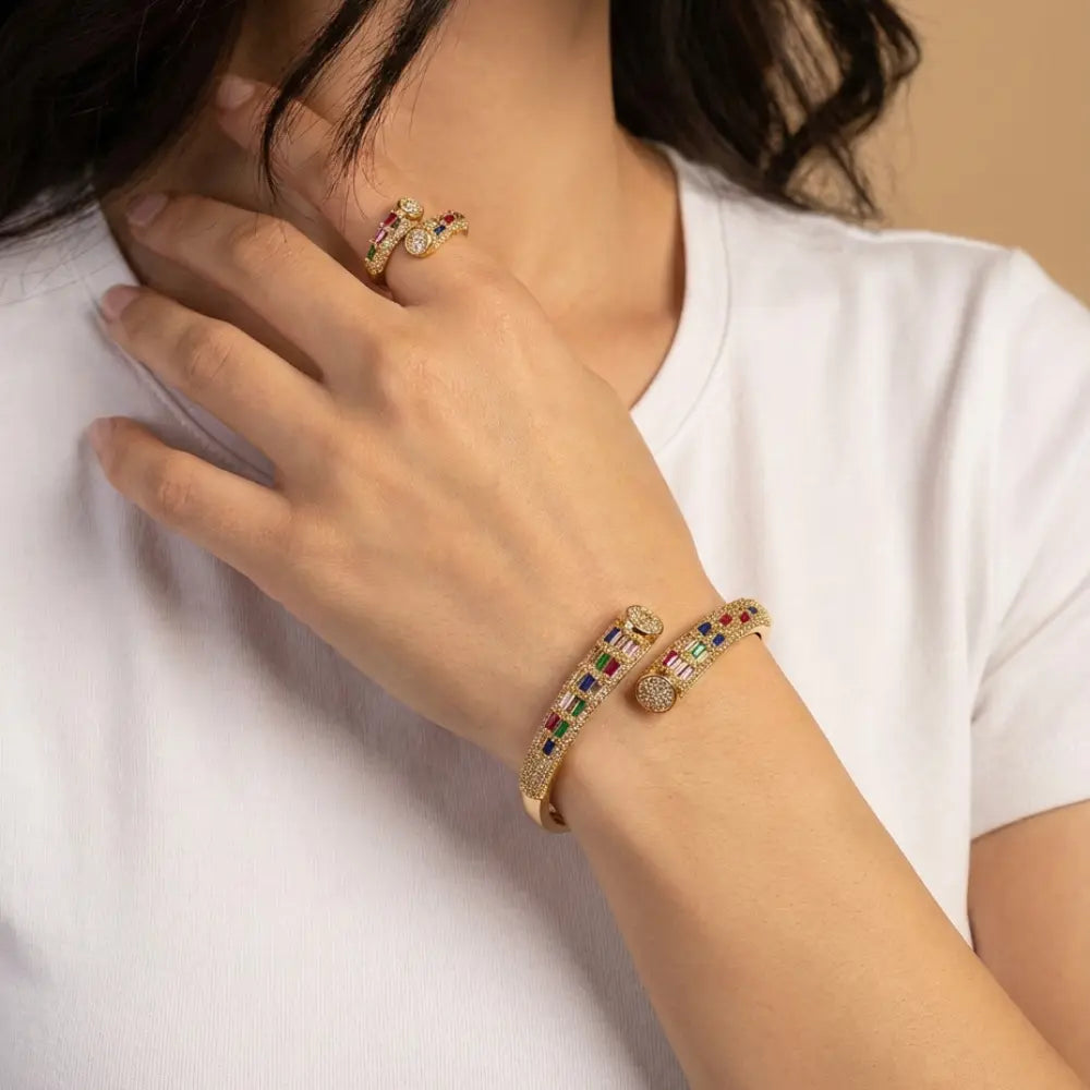 Close-up of a hand wearing a ring and bracelet with colorful gemstones on a white background