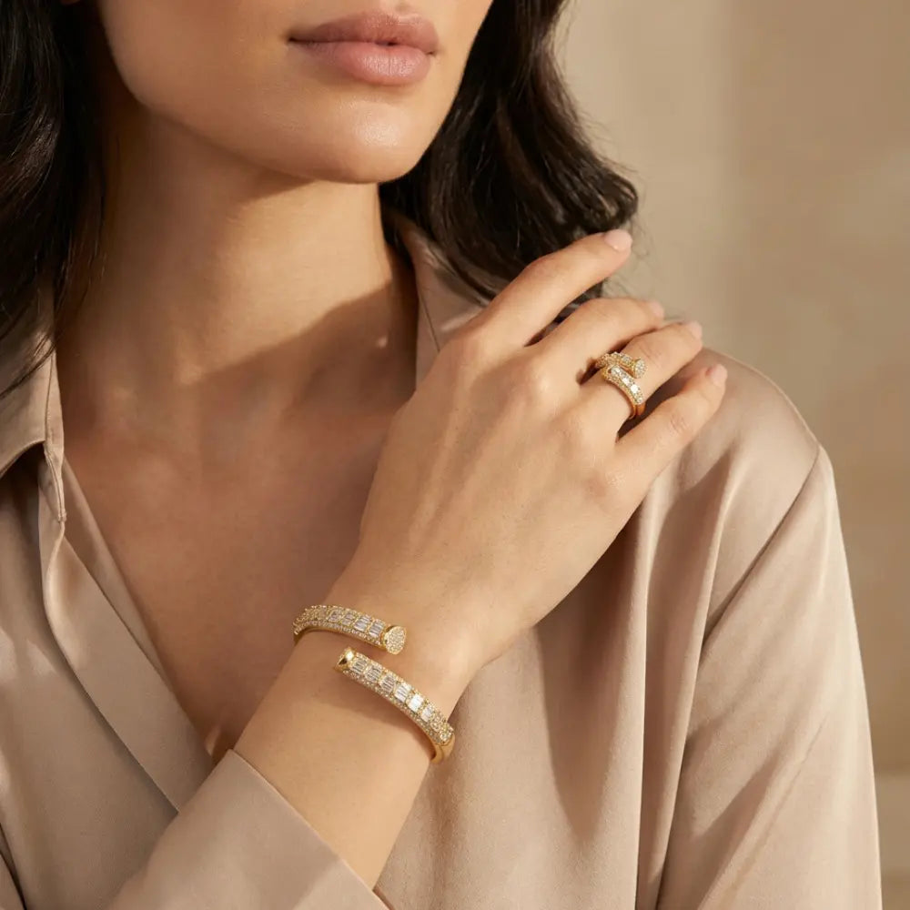 Woman wearing gold jewelry including a bracelet and ring, with a neutral background