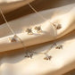 Close up of a luxury 18k gold plated necklace and matching stud earrings set featuring five sparkling star charms paved with clear zirconia on smooth satin.
