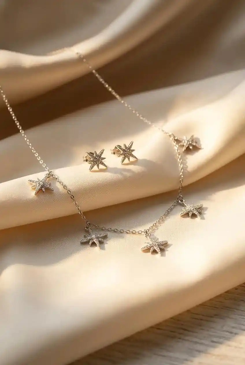 Close up of a luxury 18k gold plated necklace and matching stud earrings set featuring five sparkling star charms paved with clear zirconia on smooth satin.