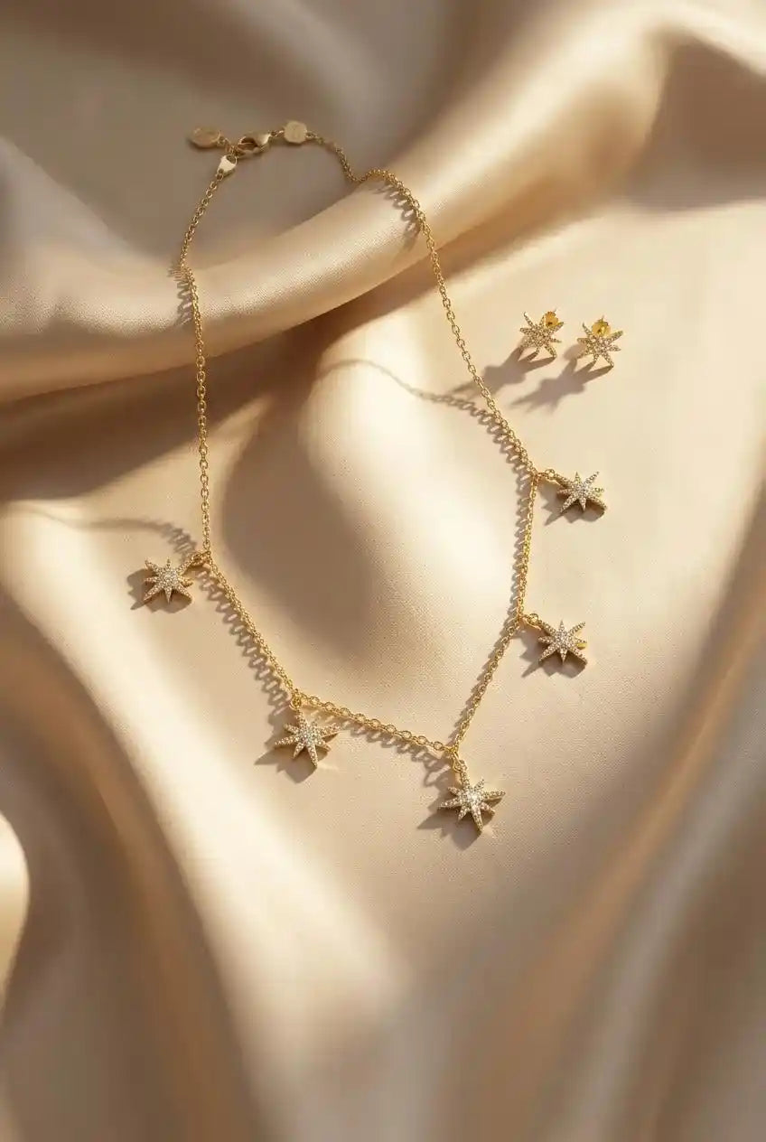 Close up of a luxury 18k gold plated necklace and matching stud earrings set featuring five sparkling star charms paved with clear zirconia on smooth satin.