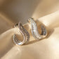 Silver hoop earrings with clear gemstones on a beige fabric background