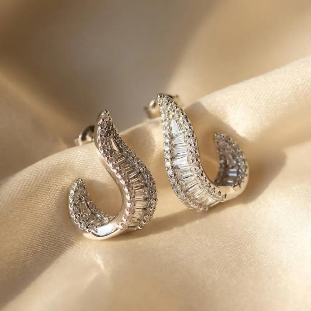 Silver hoop earrings with clear gemstones on a beige fabric background