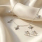 Close up of an elegant silver necklace and matching stud earrings set featuring five sparkling star charms paved with clear zirconia on soft ivory satin.