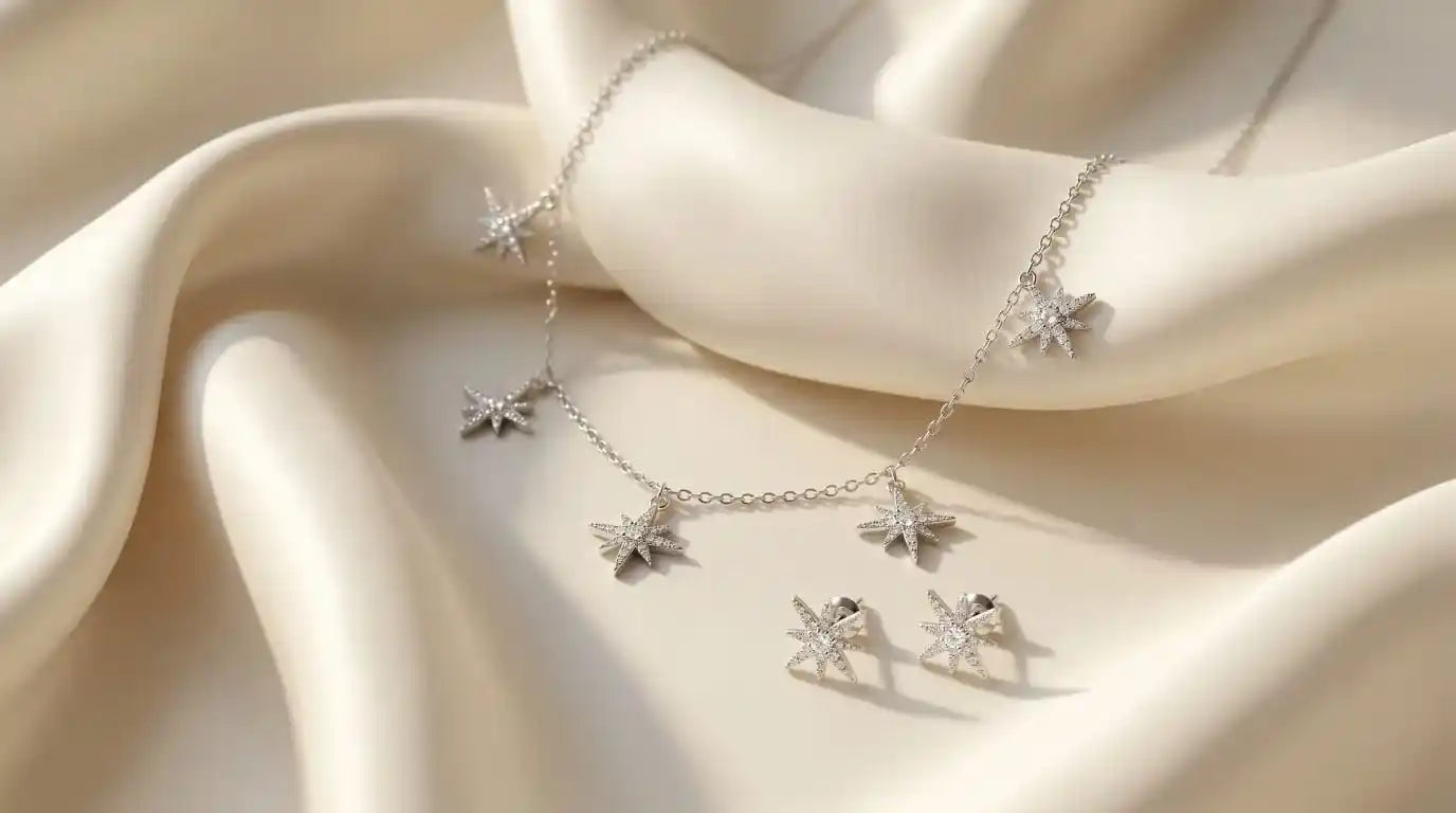 Close up of an elegant silver necklace and matching stud earrings set featuring five sparkling star charms paved with clear zirconia on soft ivory satin.